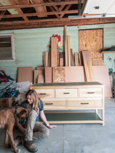 Woman and boxer dog sitting in a messy garage in front of a newly constructed dresser. She’s clearly lost her mind.