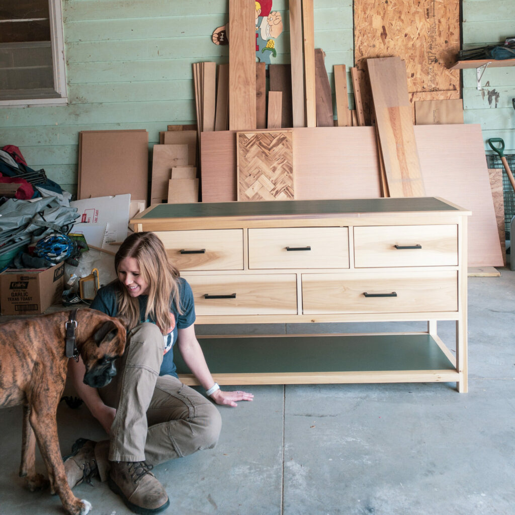 Woman and boxer dog sitting in a messy garage in front of a newly constructed dresser. She’s clearly lost her mind.