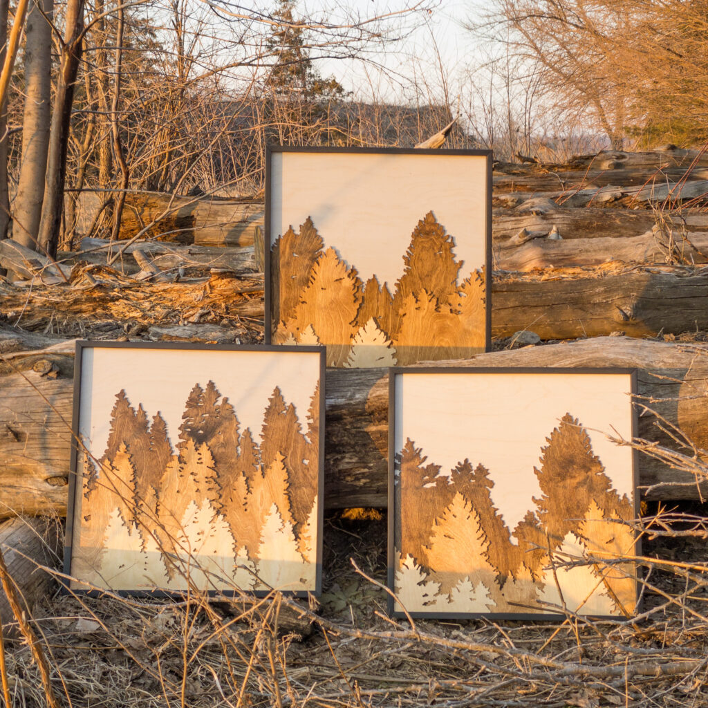 Three signs with layered pine trees. Back layer is dark brown, middle layer is medium brown, and front layer is light wood tone.