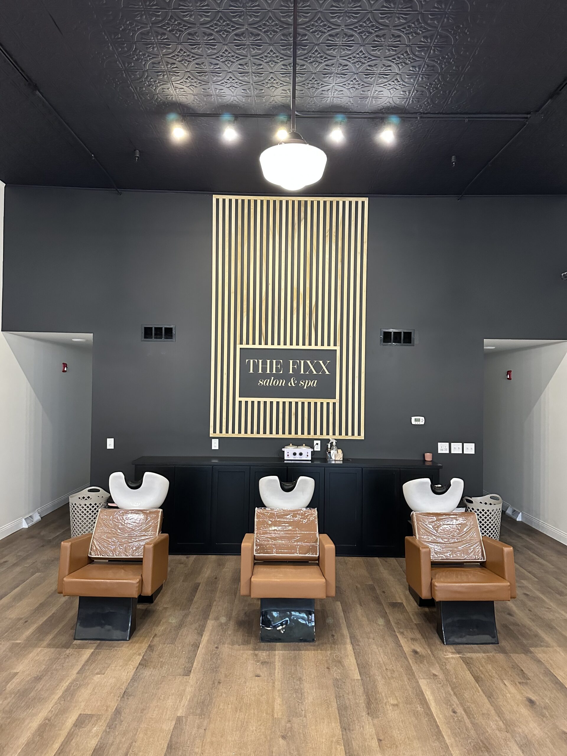 Black wall with natural wooden boards framing a sign that says The Fixx Salon and Spa
