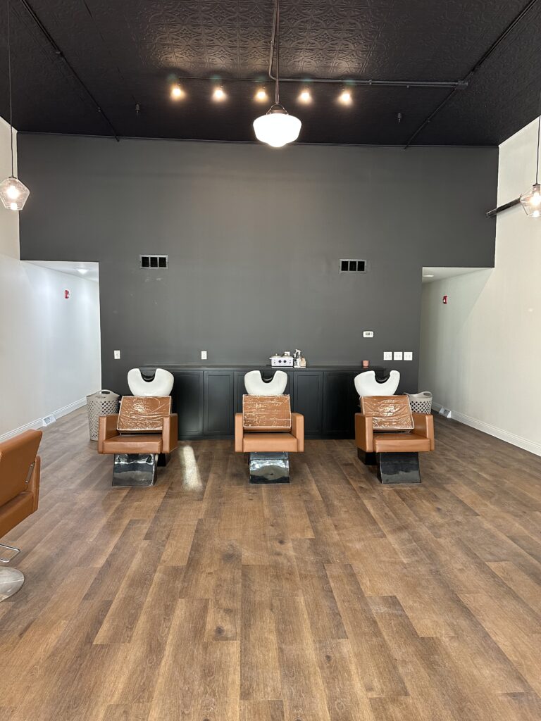 3 brown leather salon chairs in front of a large black wall