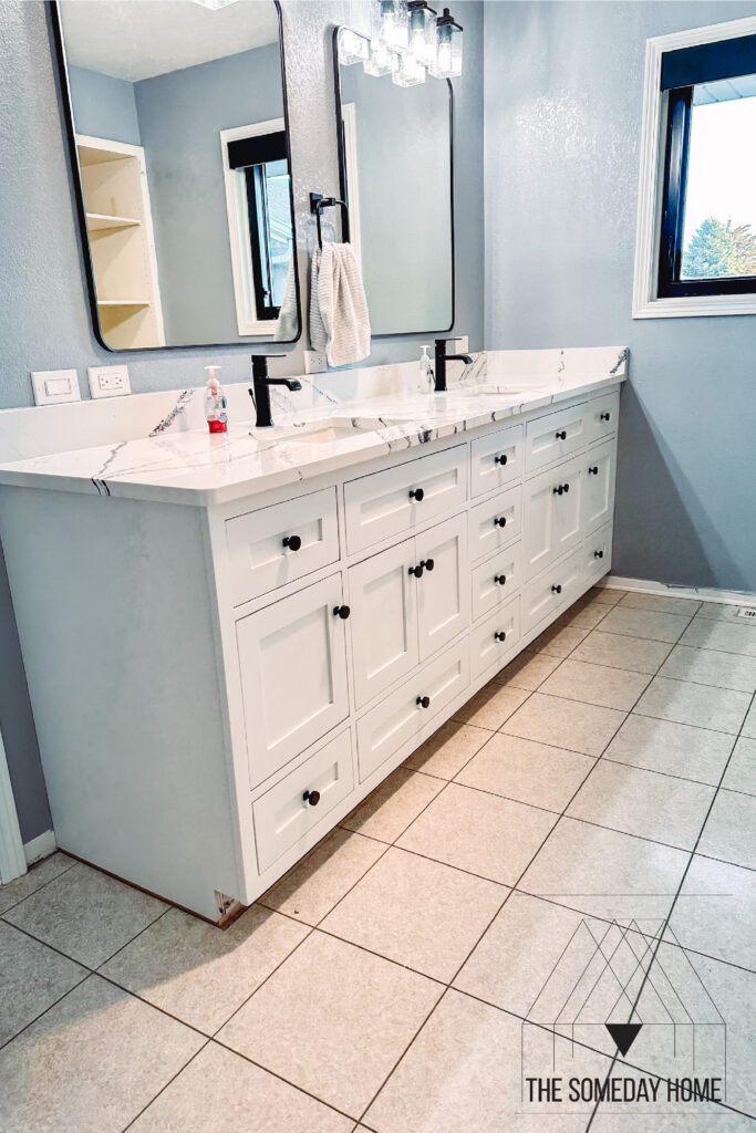 White double vanity with black faucets and black hardware, in a blue bathroom with cream colored tile