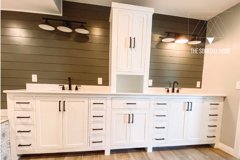 all white double vanity with a center storage tower, black drawer pulls, and black faucets.